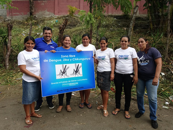 Los voluntarios de Monte Verde con un rótulo declarando que Monte Verde está libre de las enfermedades transmitidas por el mosquito Aedes aegypti.